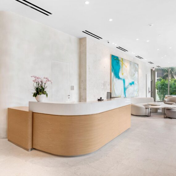 La Clara Palm Beach reception area with custom curved oak and stone desk and upholstered lounge seating manufactured by A Squared Design Studio.